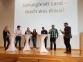 7 Personen an Stehtischen vor Leinwand