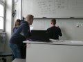 Personen in Klassenzimmer vor Tafel