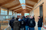 Personen stehen in einer vorwiegend aus Holz bestehenden Halle