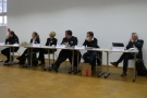 Sechs Personen sitzen nebeneinander an langem Tisch