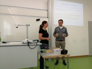 Zwei Personen stehen neben Pult in Klassenzimmer